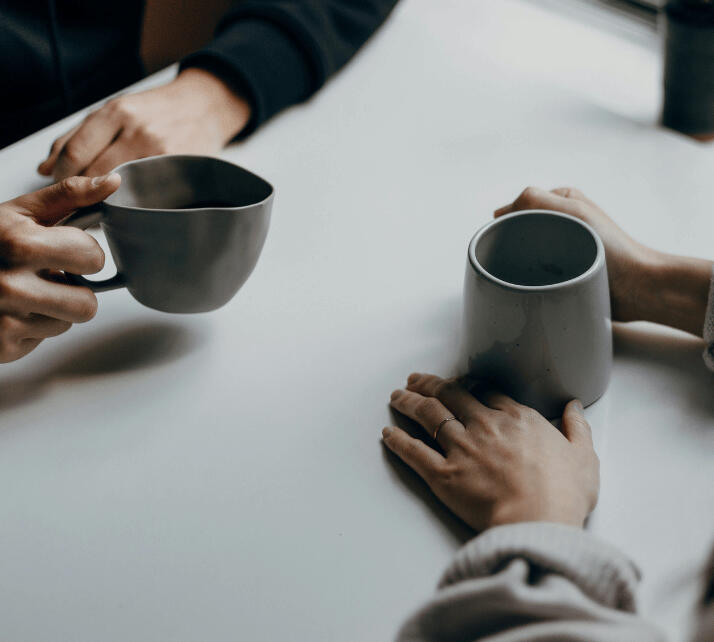 close up of hands on cups over a table at what seems like a coffee shop